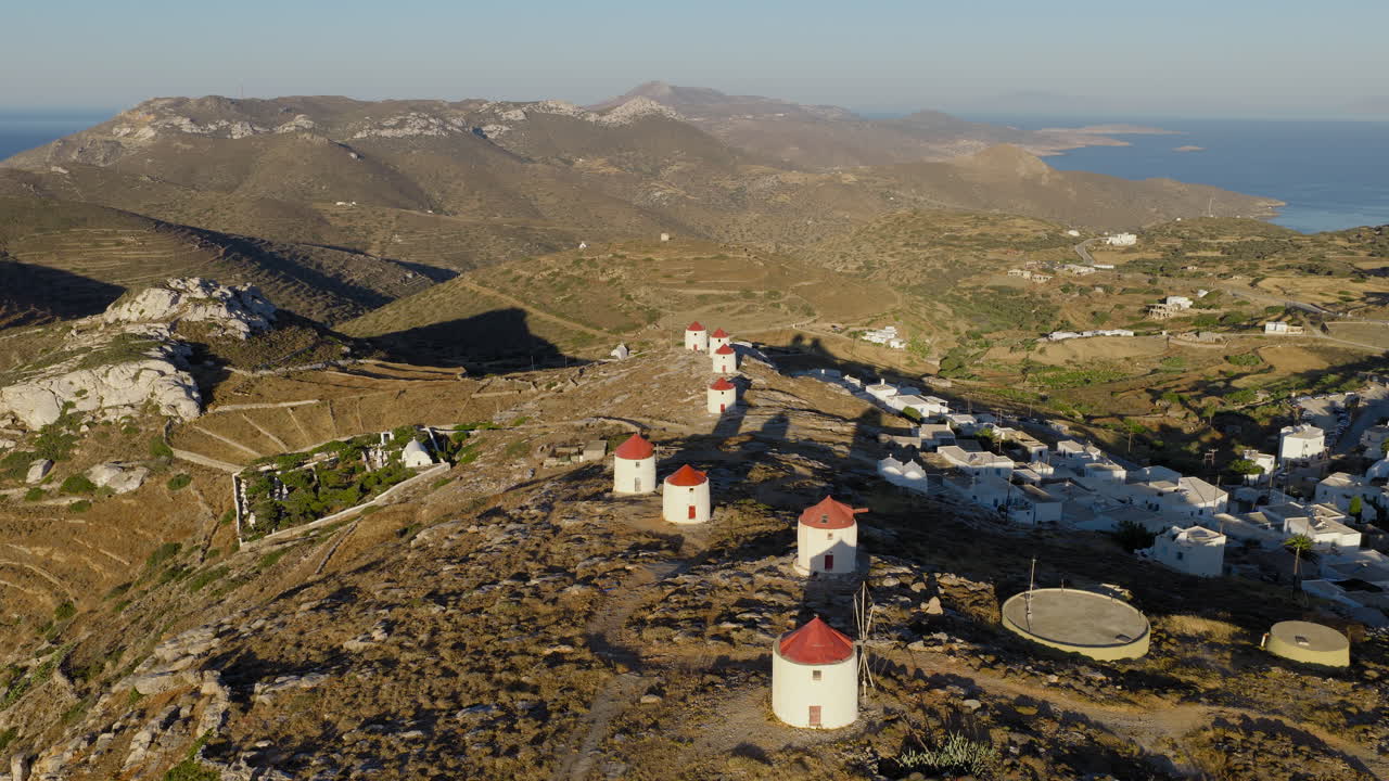 Windmills in Chora, Amorgos island during sunrise surrounded by Aegean sea, Establishing drone shot