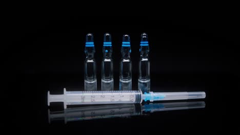 close-up of syringe and ampoules with vaccine against coronavirus. showing sample of medicine on black background, vaccination against covid-19, laboratory research concept