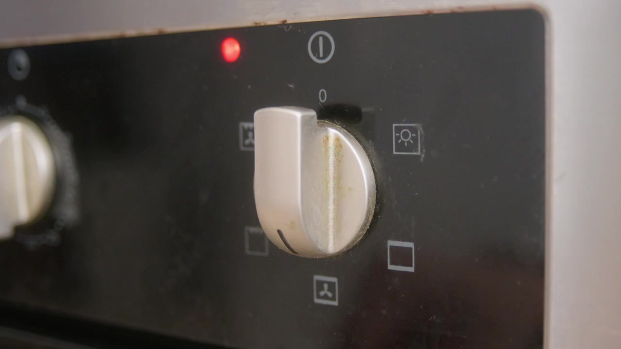 Close-up of a hand operating the different modes dial on an old electric kitchen oven. A mode is selected and the oven operation light activates.