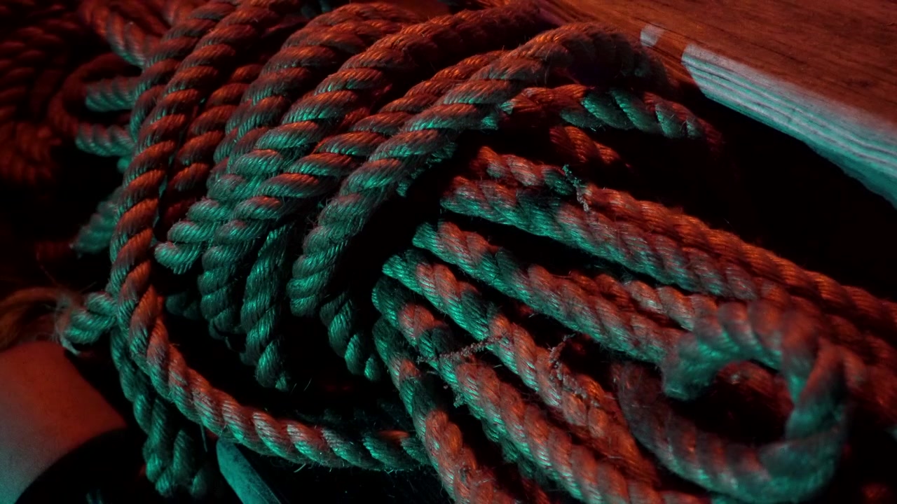 Corda arrotolata giace su un ponte di legno illuminato dalla luce delle torce.