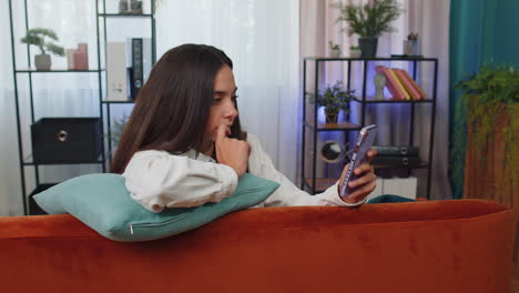 Portrait-of-adult-girl-sitting-on-sofa,-using-smartphone-share-messages-on-social-media-application