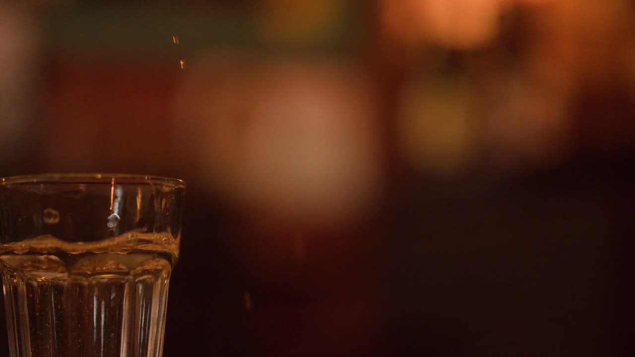 Acqua frizzante e limpida versata in un bicchiere su uno sfondo sfocato e caldo da pub