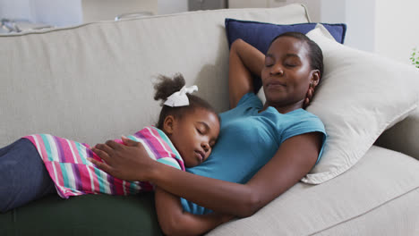 happy african american mother and daughter lying on sofa and relaxing with eyes closed