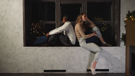 Black-man-and-white-woman-sit-back-to-back-on-windowsill