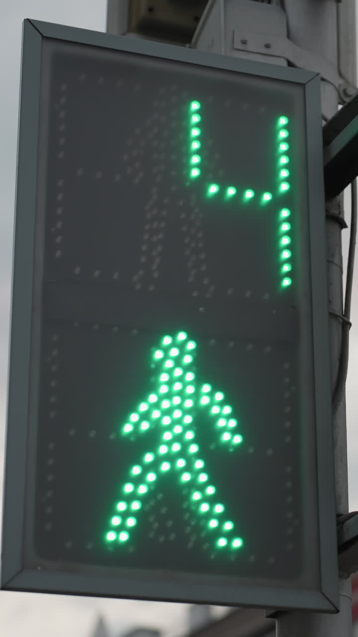 vista cercana de un semáforo digital que muestra una cuenta atrás con una señal de peatones verde, con un edificio de la ciudad roja y un cielo nublado