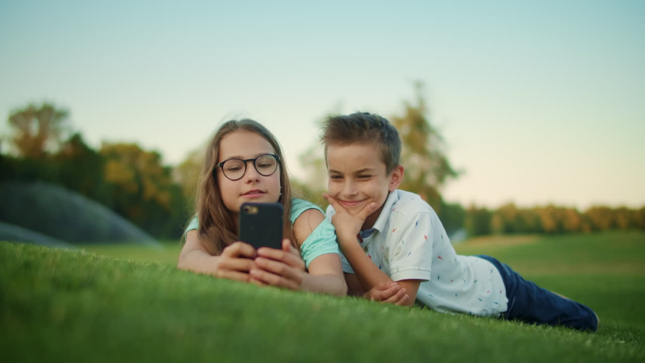 Siblings lying on grass in field with smartphone