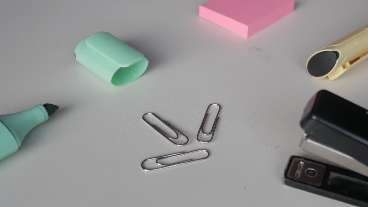Top-down view of metallic paper clips and a mint green marker placed on a white minimalist workspace