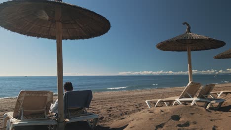 Man-relaxing-at-a-sunny-beach-with-parasol-and-chairs