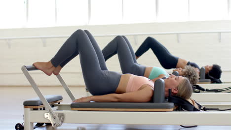 three women are exercising on pilates reformer machines in bright studio