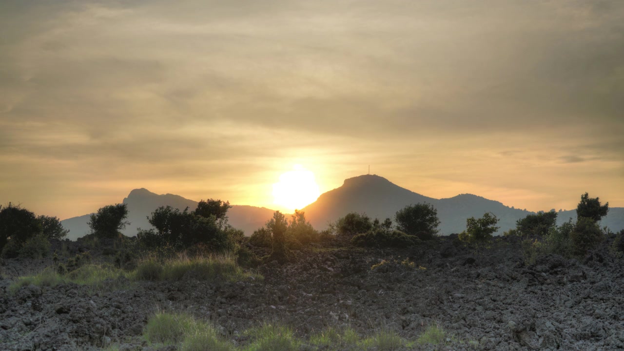 Pôr do sol sobre paisagem vulcânica com pico de montanha distante