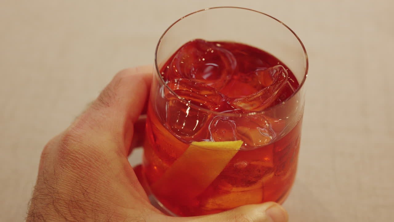Primo piano di un uomo che tiene in mano un bicchiere da cocktail pieno di ghiaccio e una guarnizione di agrumi