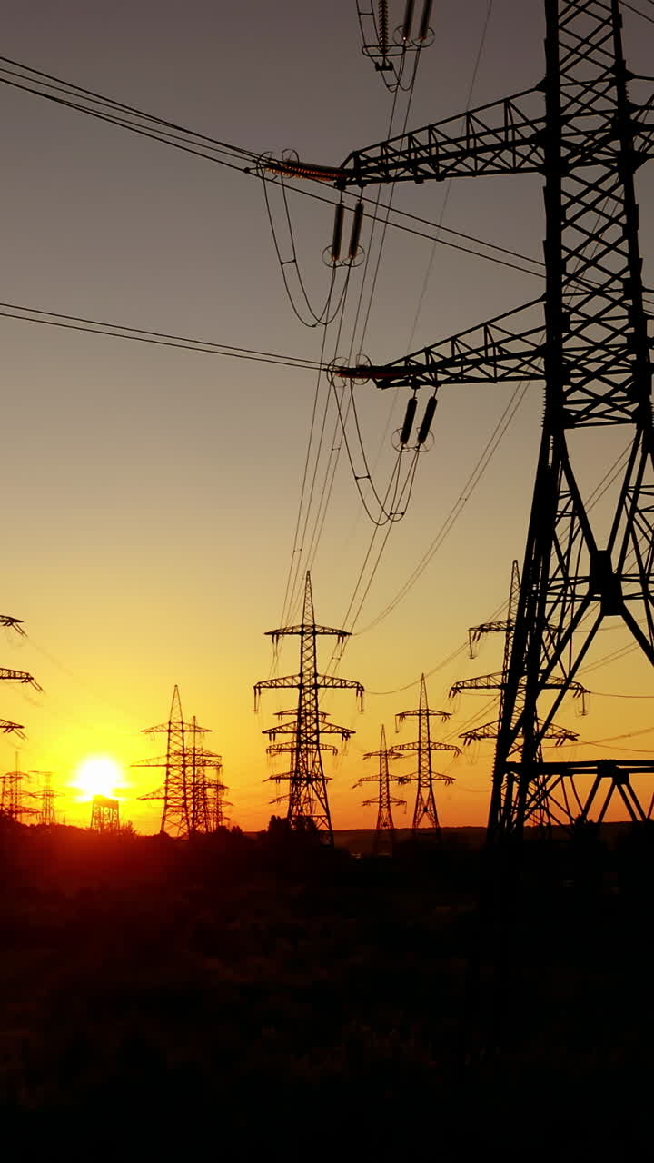 Transmission electric on towers at sunset. High-voltage power lines. Electrical pylons on the orange sky background. Drone view. Camera rising up. Vertical video
