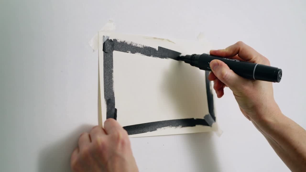 Drawing hands finishing black border on taped sheet on wall, using marker and tape, short sleeves