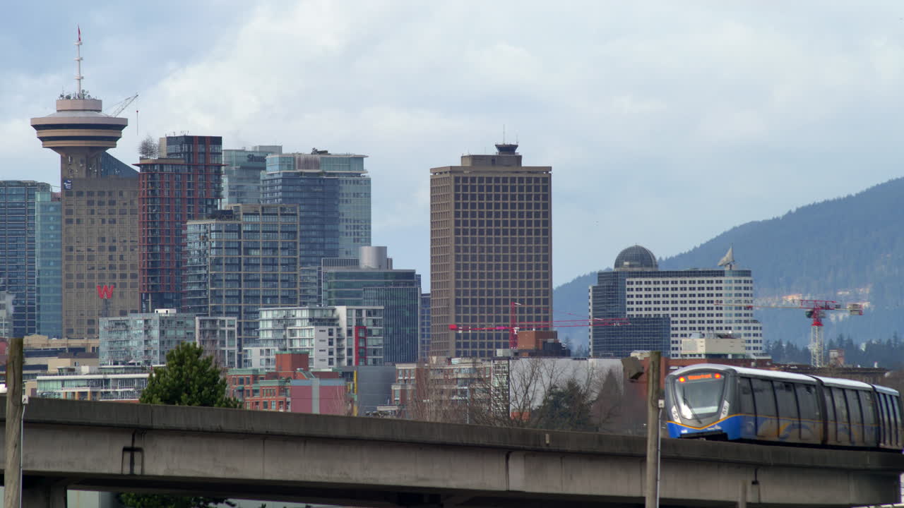 Ampia inquadratura di un treno in transito e dello skyline della città di Vancouver sullo sfondo durante una giornata nuvolosa, Canada