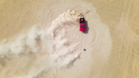 drone looking down on a red truck doing doughnuts in the desert, kicking up big clouds of sand dust