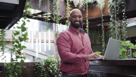 happy biracial male creative using laptop at casual office, in slow motion