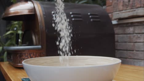 chef puts down the pizza flour into a deep plate