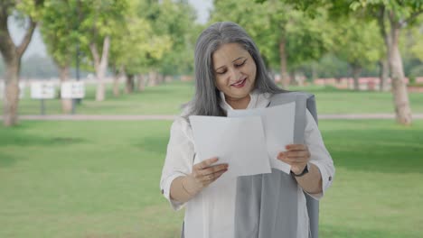 una vieja india feliz leyendo informes en el parque.