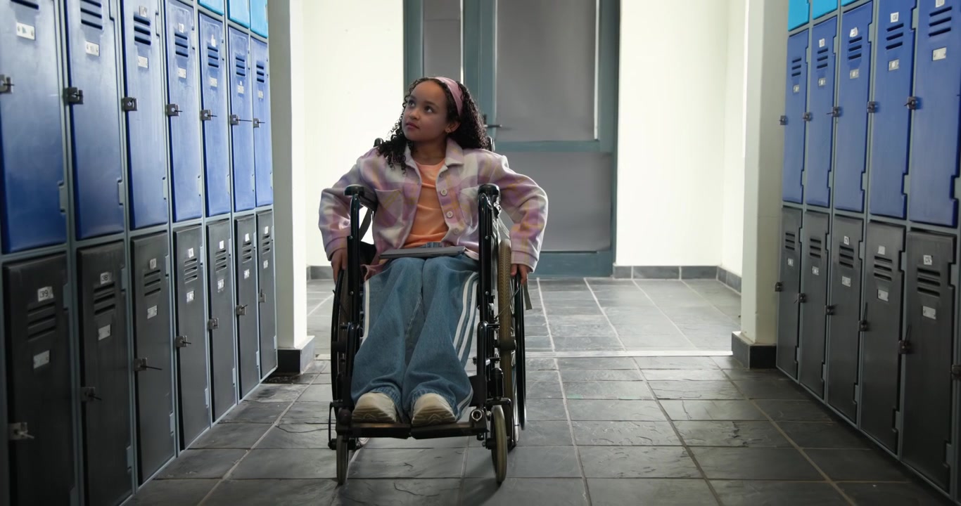 African teen girl pushing wheelchair ahead from closed door, scanning blue lockers heading to class