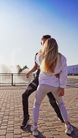 modern dancers are dancing in the street. urban lifestyle. hip-hop generation. boy's and girl's emotional moves on the video. paving stones and young dacing couple at fontain background. vertical video