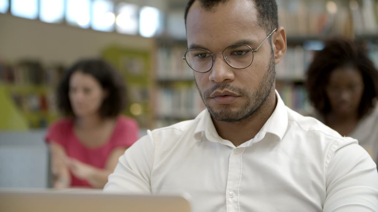 captura de pantalla de un joven enfocado que usa una laptop en la biblioteca