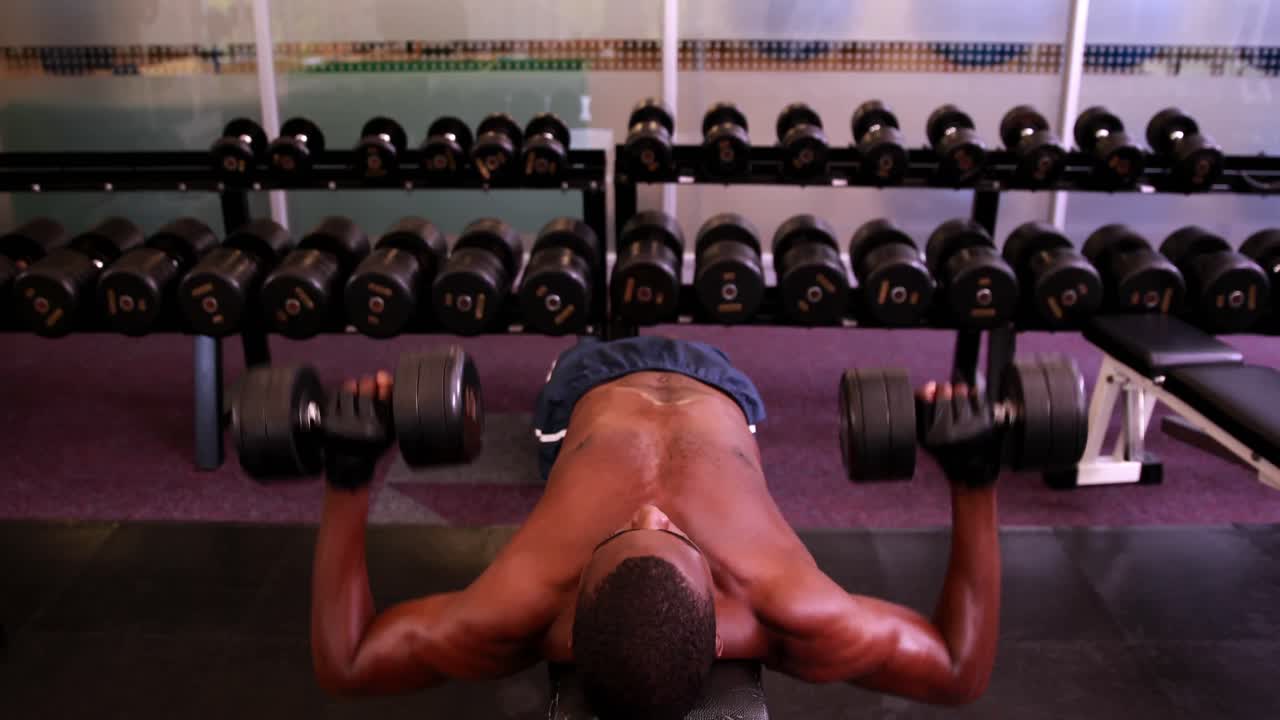 hombre sin camisa levantando pesas acostado en un banco