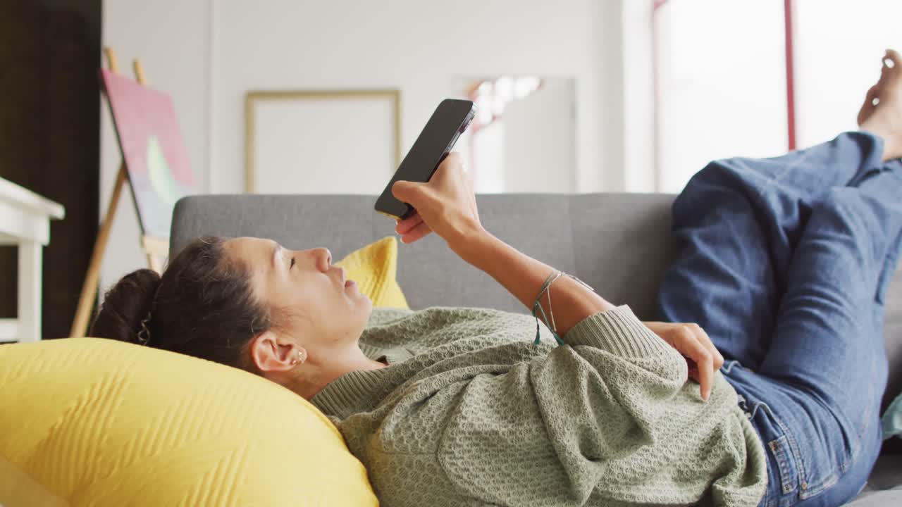 video de una feliz diseñadora biracial usando un teléfono inteligente y relajándose en el estudio