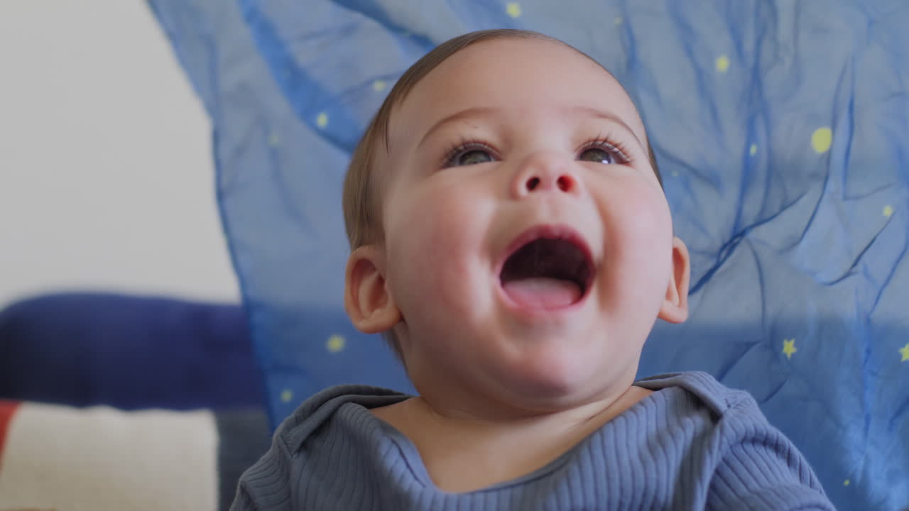 bebé sonriendo y riendo jugando con una seda azul con estrellas amarillas en cámara lenta