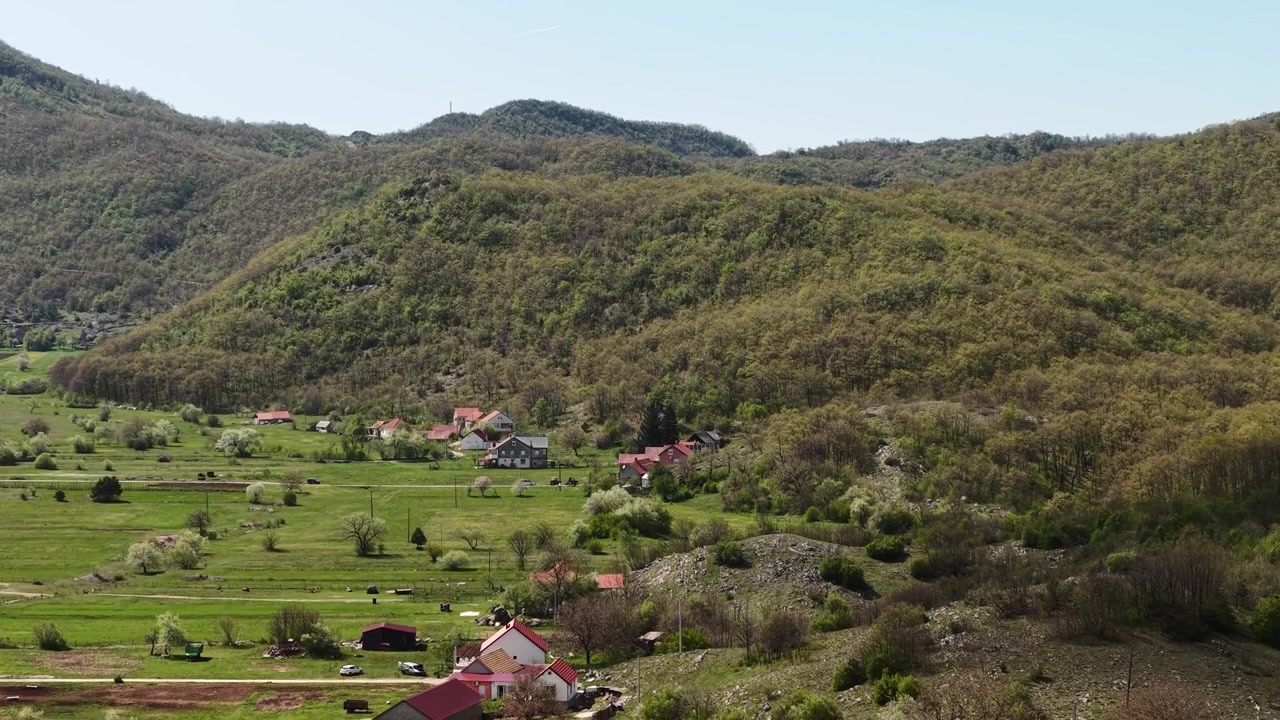 Ripresa aerea di un villaggio sotto le colline montuose del Montenegro, campi agricoli e case.