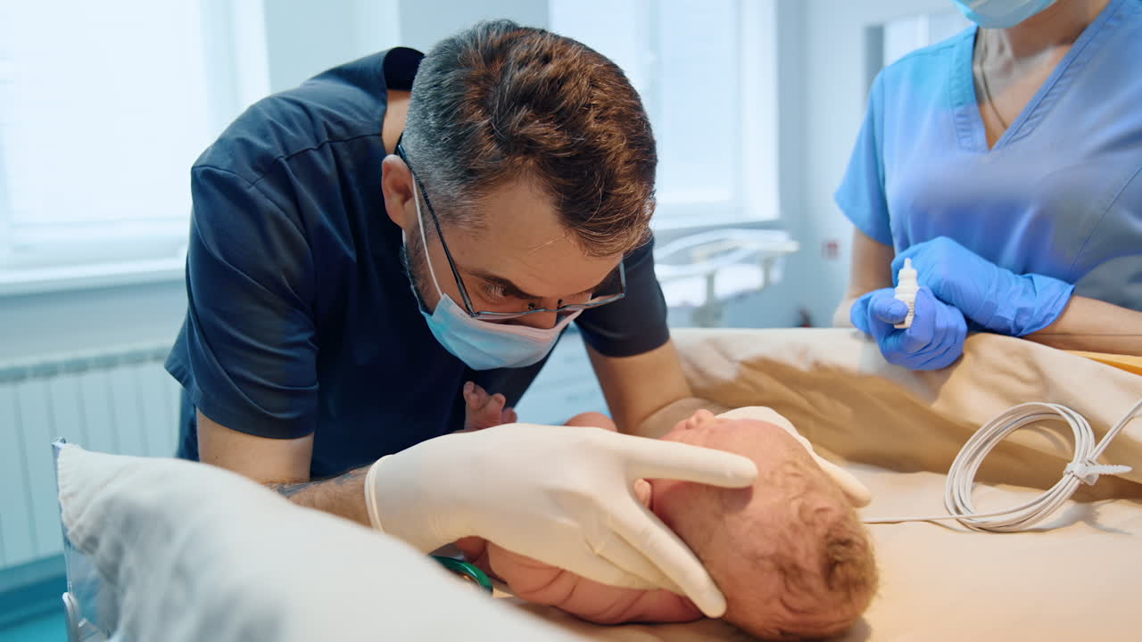 Male doctor wearing eyeglasses and mask looks closely at a child. Neonatologist examines newborn baby.