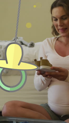 animation of dummy and yellow spots over caucasian pregnant woman holding baby shoes