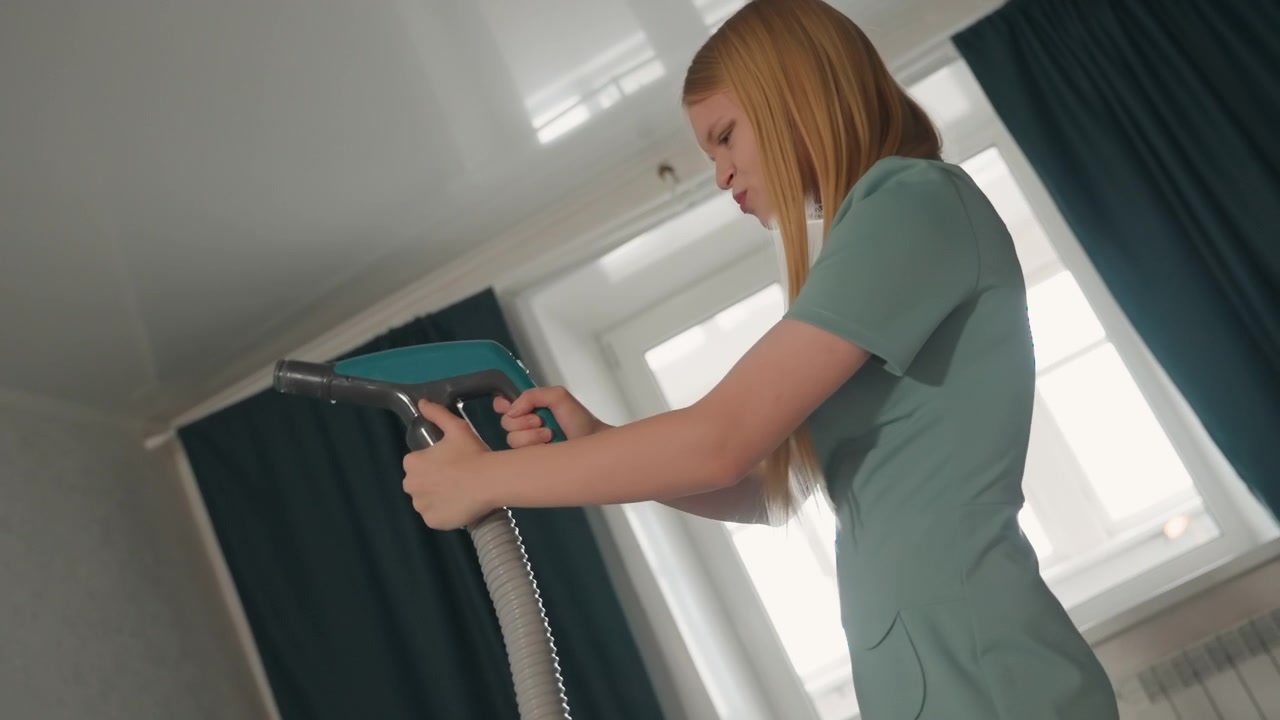 Donna bianca sicura di sé stira a vapore le tende a casa per le pulizie in un appartamento moderno e luminoso, sorride e si allunga verso l'alto con un vaporizzatore portatile, rinfrescando tessuti e tappezzeria, routine igienica.