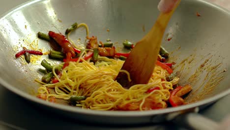 cu slow motion cook prepares noodles pasta in frying pan in oil with fresh vegetables