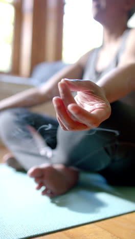 vertical video of focused senior biracial woman meditating with incense sticks at home, slow motion