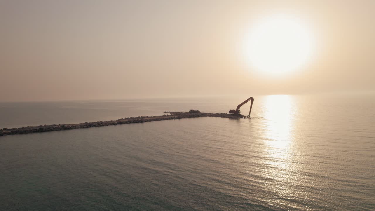 máquina excavadora de largo alcance esperando recibir piedras para construir un rompeolas en el mar, toma mágica durante la puesta de sol