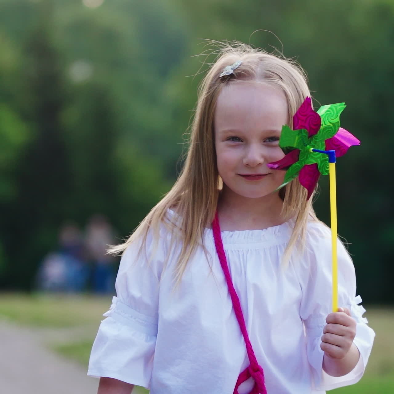 Beautiful little girl with colorful toy in the park. Pretty young child in white blouse looking at camera joyfully.