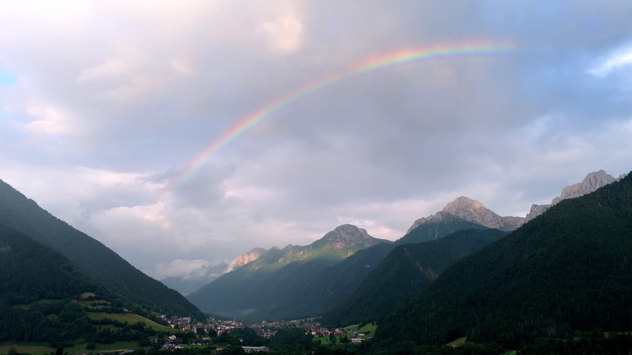 Aerial drone view of a fairytale landscape in Val di Scalve, Italian Dolomites and Alpi Orobie, featuring a vibrant rainbow arching over lush alpine valleys and rugged mountain peaks