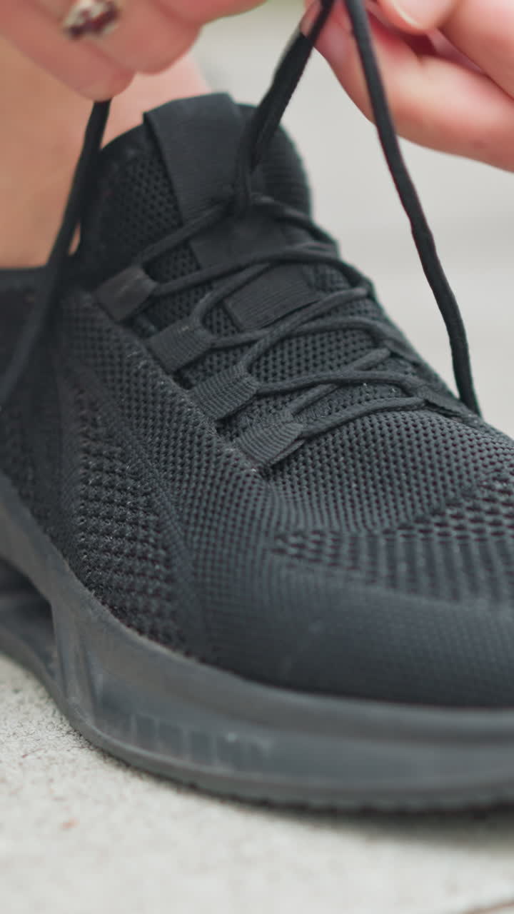 Vista sfocata di una ragazza con scarpe da ginnastica nere che si allaccia le scarpe, l'attenzione è sulle sue scarpe mentre si prepara per una corsa, mostrando uno stile di vita attivo e una routine di fitness.