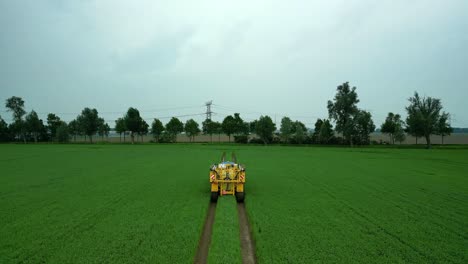 blue tractor with a folded yellow field sprayer drives through a green grain field