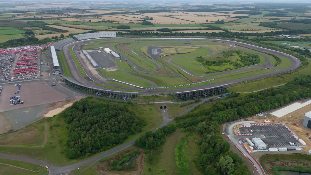 Drone cinematic overhead aerial footage of motorsport circuit with event facilities, grandstands and cars in car park Corby England UK