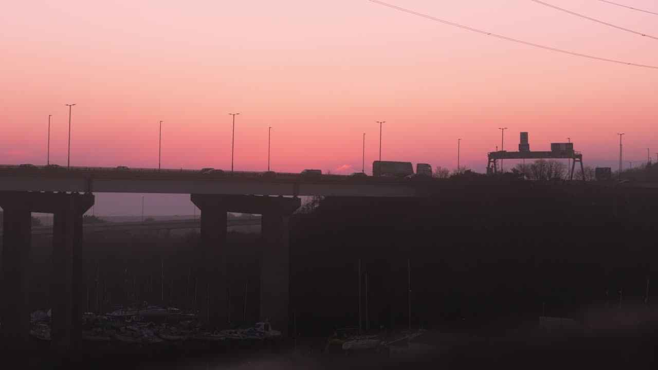 Slow Motion of Cars and Lorries Travelling Along M4 Motorway Bridge at Sunset with Direction Signs and Orange Glow on Horizon. ProRes 4K.