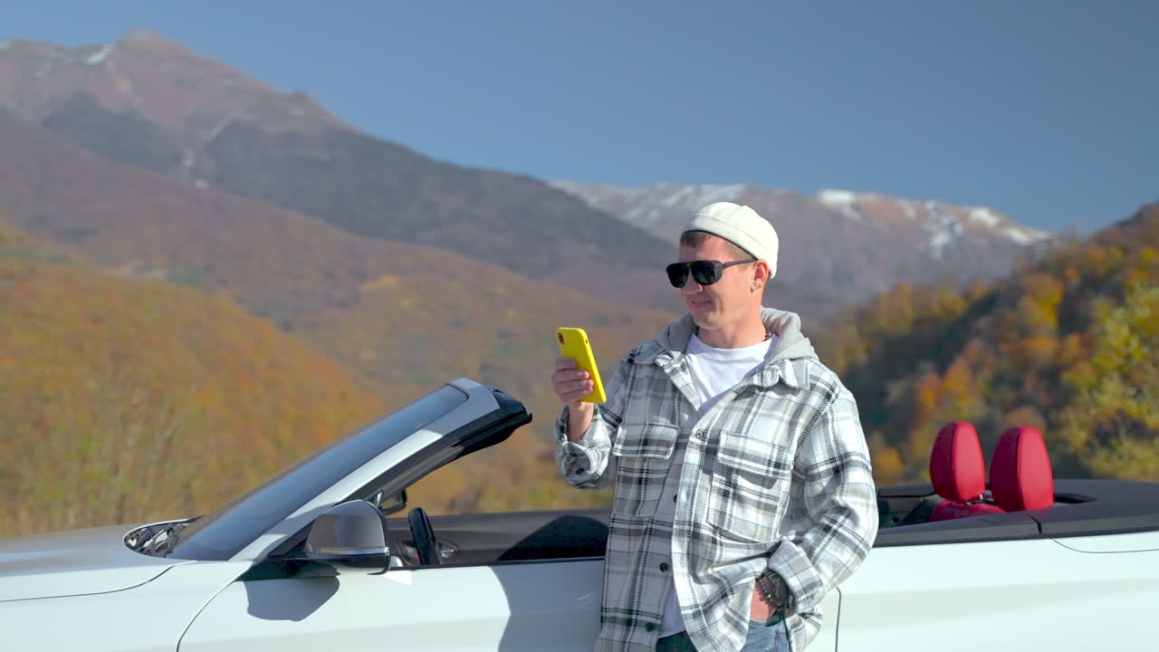 산에서 컨버터블 자동차에서 전화를 사용하는 남자