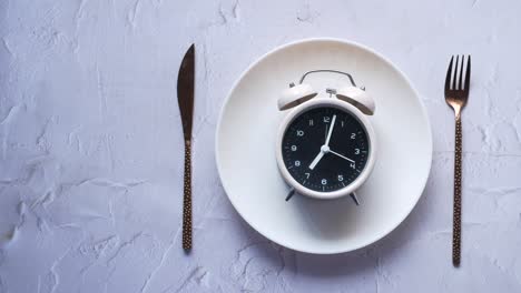 alarm clock on plate on wooden table, top view