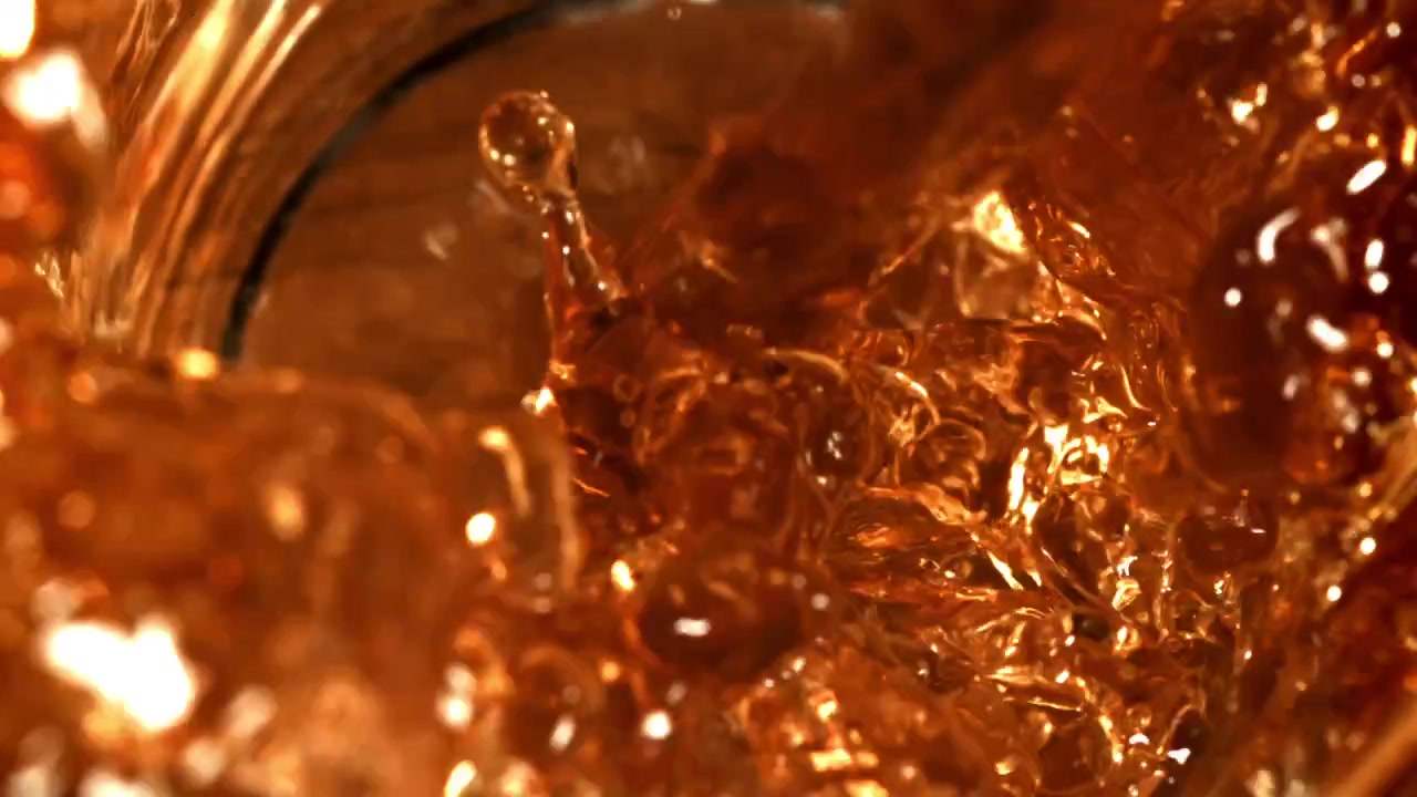 Super slow motion di liquido ambrato che si versa e schizza in un bicchiere