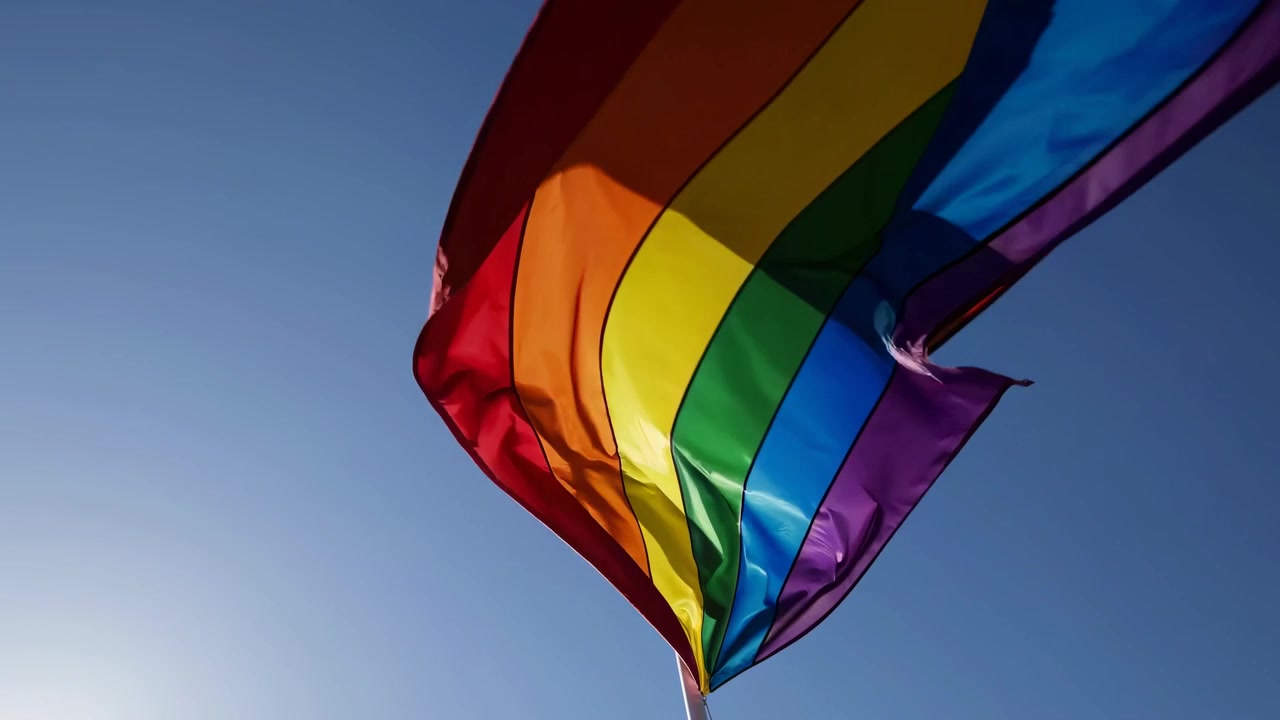 Vibrant LGBTQ+ Pride Flag Waving in the Wind Against a Blue Sky