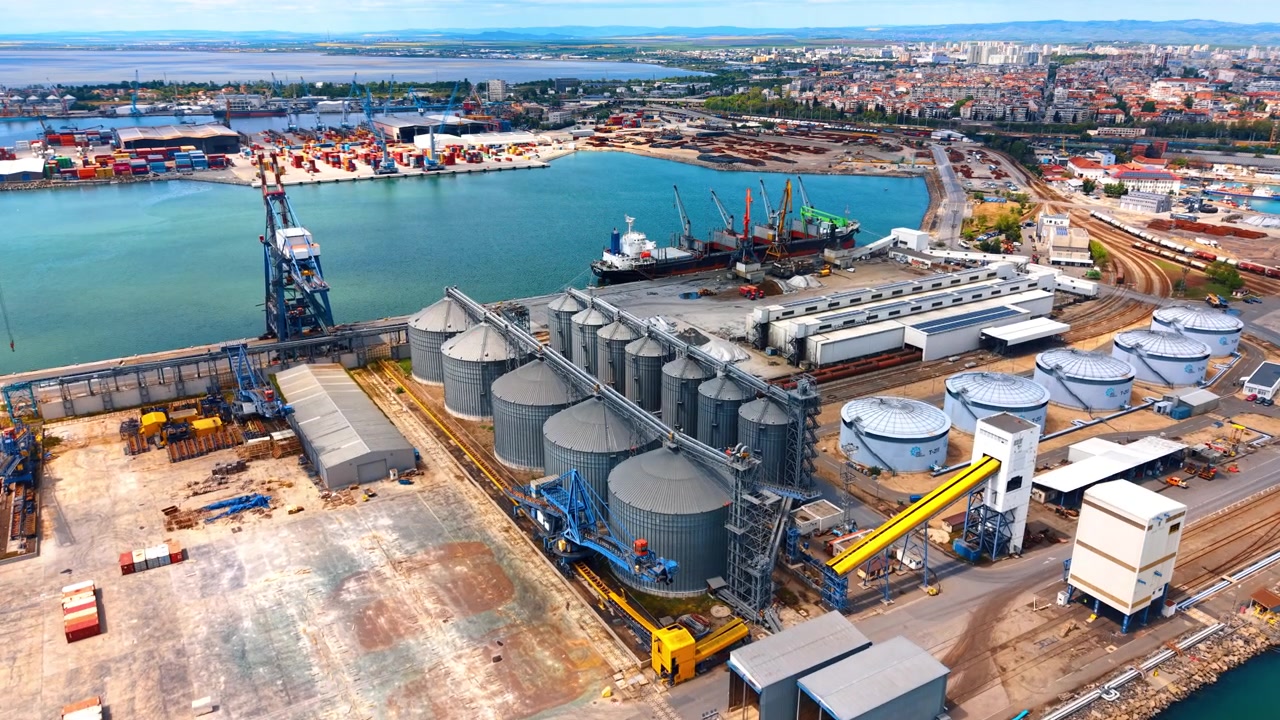 Luftaufnahme eines Getreideterminals und von Silos im Seehafen. Draufsicht auf einen großen industriellen Getreidespeicherkomplex mit Metallsilos, Eisenbahngleisen und Frachtdocks am Seehafen.
