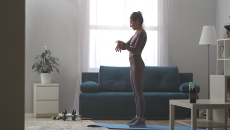 sportswoman-is-training-alone-in-living-room-viewing-smartwatch-and-squatting-with-jumps-home-fitness-at-weekends-sporty-lifestyle