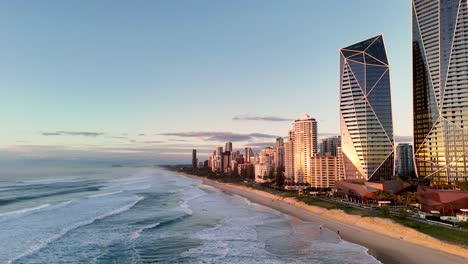 drone captures gold coast's beachfront skyline at sunrise, highlighting waves, skyscrapers, and serene morning light