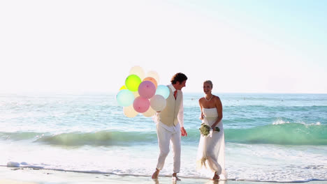 newlyweds laughing and playing with balloons on the beach