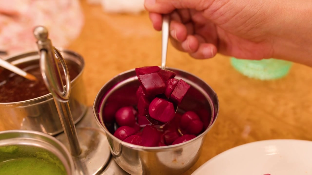 Close-up of a hand using a spoon to scoop sirke wale pyaaz in Bangkok.